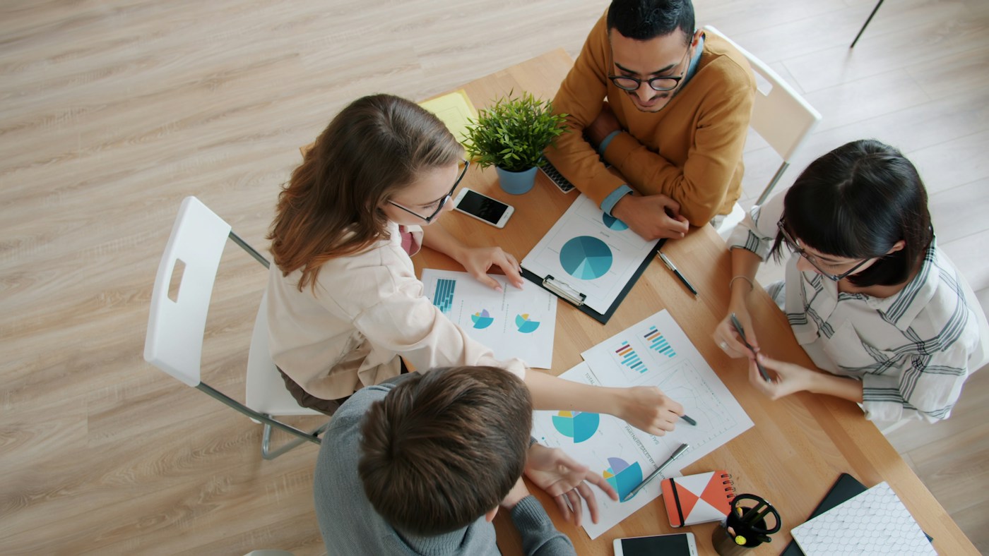 Adult colleagues collaborating around a table, discussing colorful charts and shared workplace ideas.